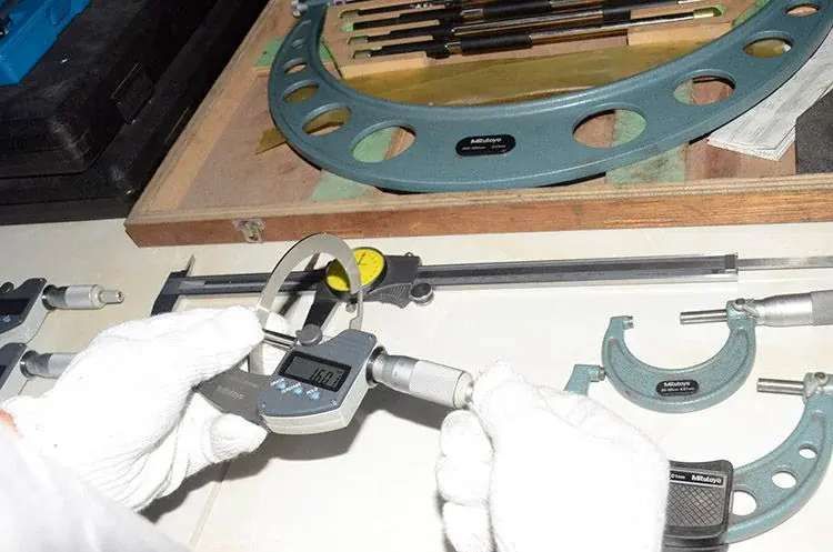 Gloved hands checking a knife with a digital micrometer
